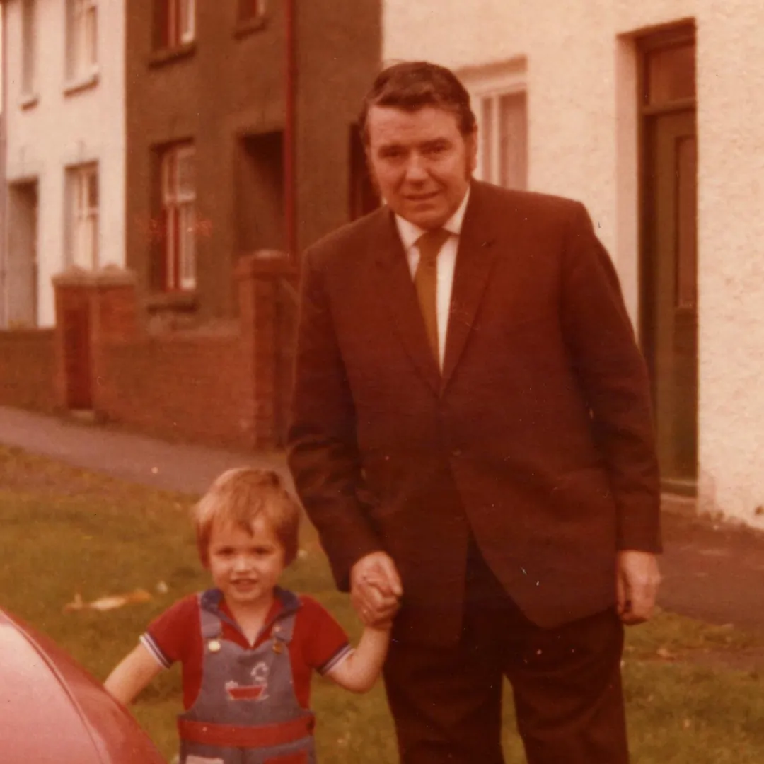 A red cast image of a young boy and his grandfather. Showing the original version, and a restored full colour version.