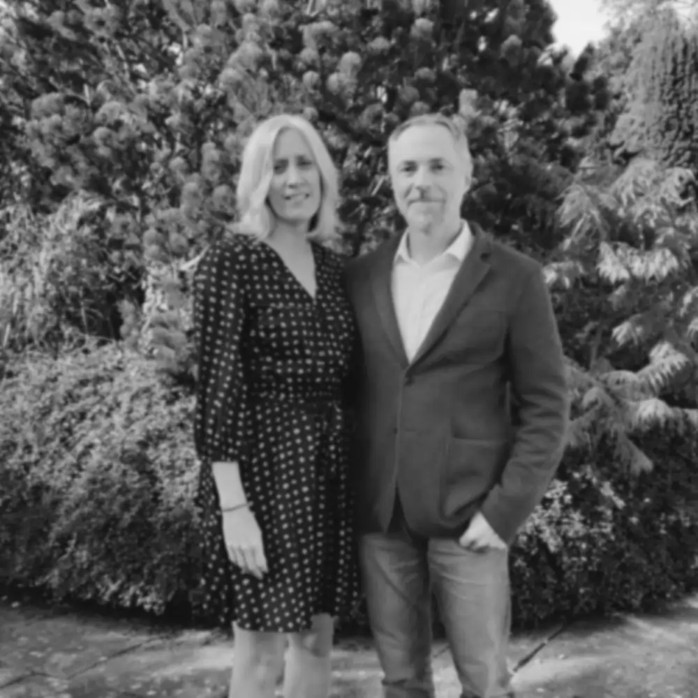 A degraded version of the recent photo of my wife and I in colour, standing in front of a bush, also shown is the restored version