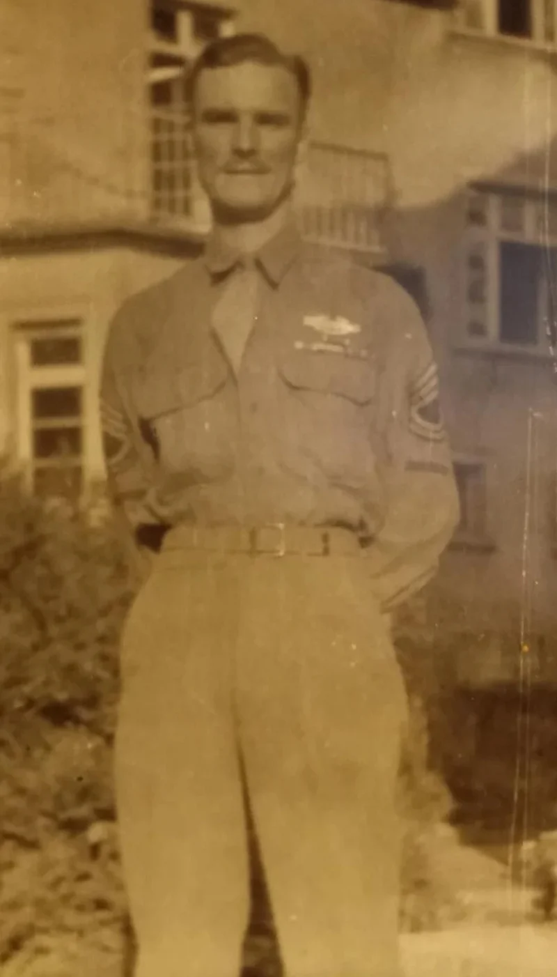 A sepia-toned World War II-era photograph of a man in a military uniform with sergeant chevrons and ribbons, standing outdoors in front of a building. The second, AI-restored version enhances the image in color, making the uniform, insignia, and man's features clearer and more vivid.