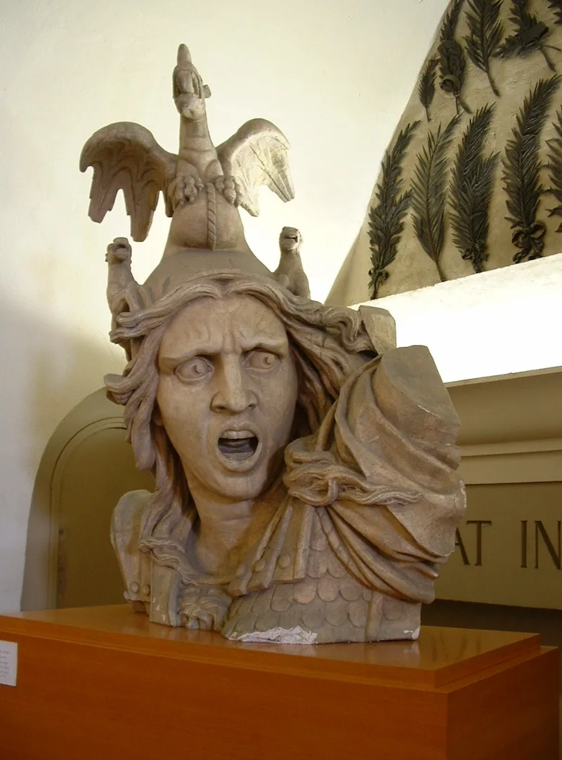 A marble bust of a figure wearing ornate armor and an elaborate winged helmet, displayed on a wooden pedestal in a museum setting. In the second, AI-generated image, the statue appears as a lifelike person with realistic coloring and texture, closely matching the pose and details of the original sculpture.