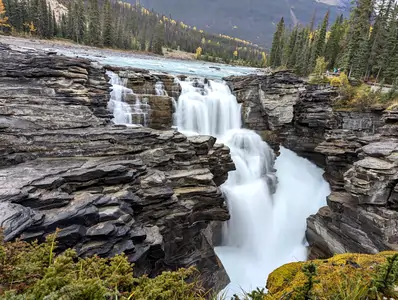 A photograph of a waterfall, the water is flowing over a rocky ledge, a long exposure has been used, so the water has a smooth appearance.