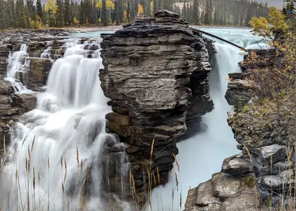A photograph of two small adjacent waterfalls, the falls are separated by a rocky outcrop. A long exposure has been used, giving the water a smooth appearance.