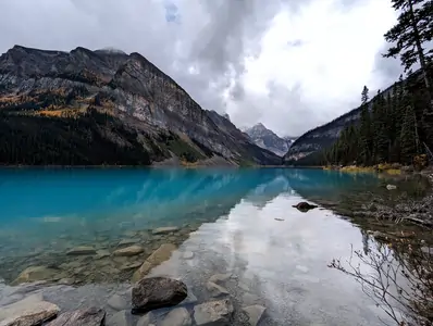 A photograph taken from the bank of a large deep-blue coloured lake. The lake is surrounded by mountains.