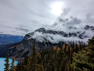 A photograph taken from a high vantage point overlooking a lake far below. In the background is a large rocky mountain. 