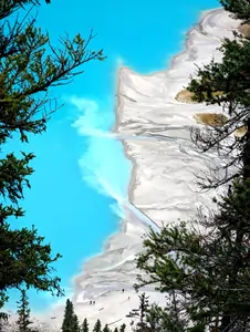 A photograph taken from a high vantage point, looking down at the shore of a deep-blue coloured lake. The shore appears to be made of a very fine grey coloured silt, and the silt can be seen seeping into the lake.